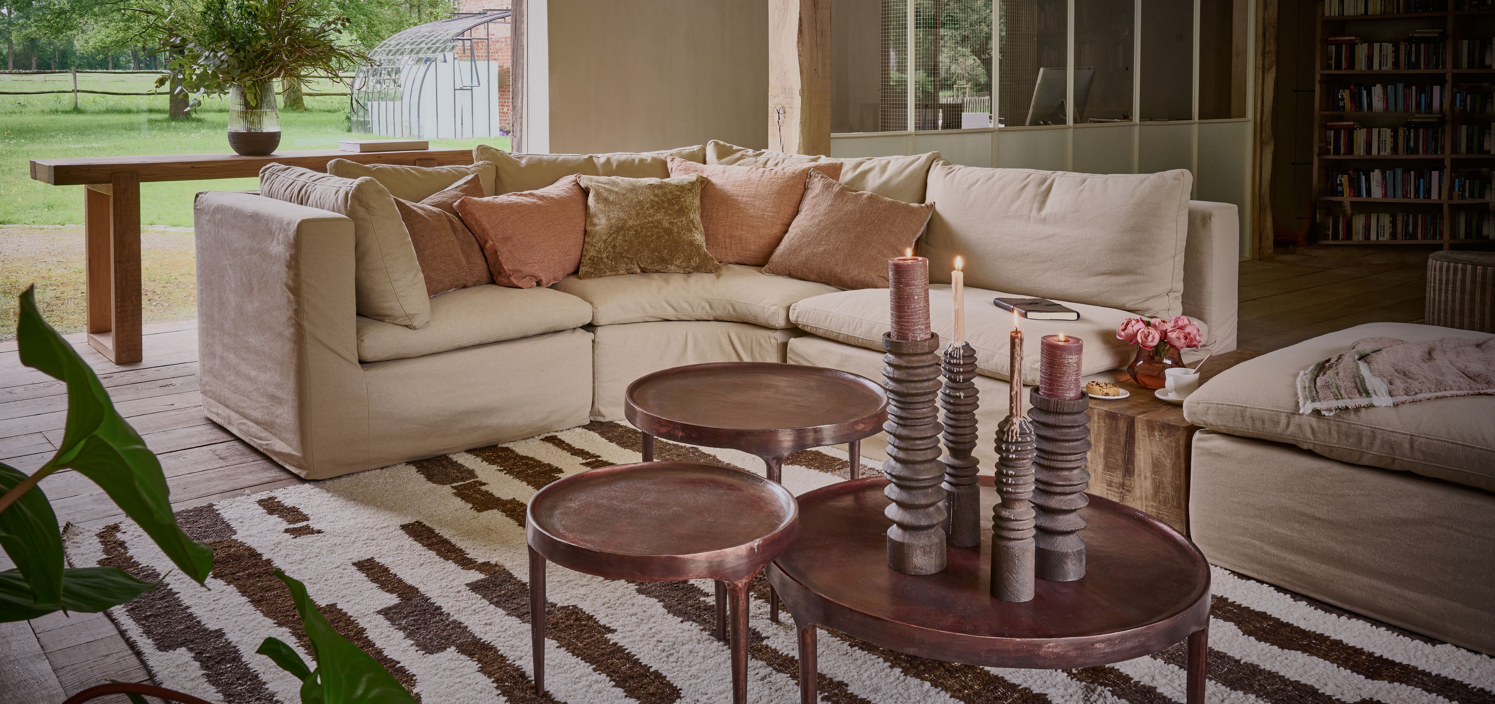A cozy living room with a large beige sofa, pink cushions, round coffee tables and tall candle holders on a striped rug