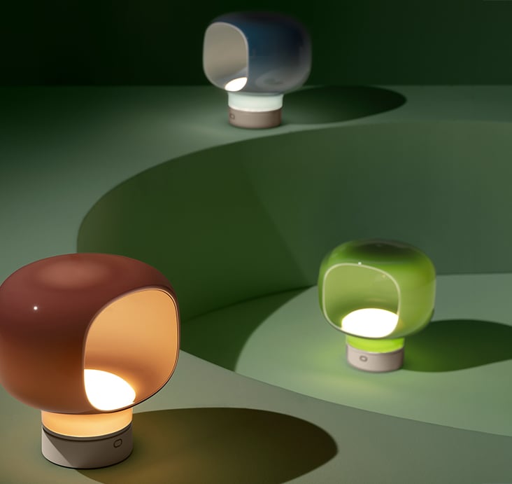 A brown and a green NasonMoretti 'Mini Technicolor' mushroom lamp glowing on a curved green surface