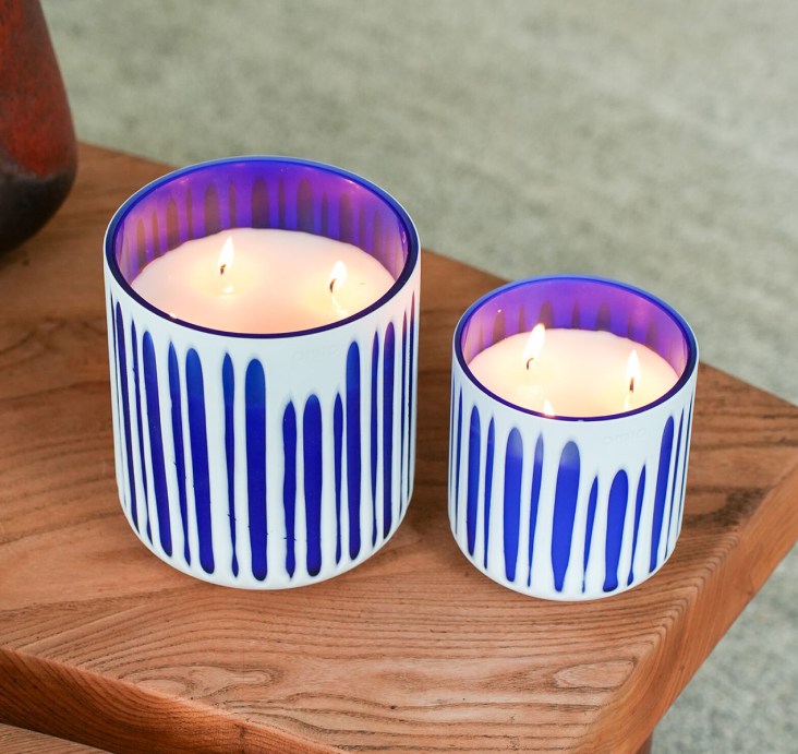 Two Onno Collection 'Cielo' candles in blue and purple striped ceramic vessels on a wooden tray
