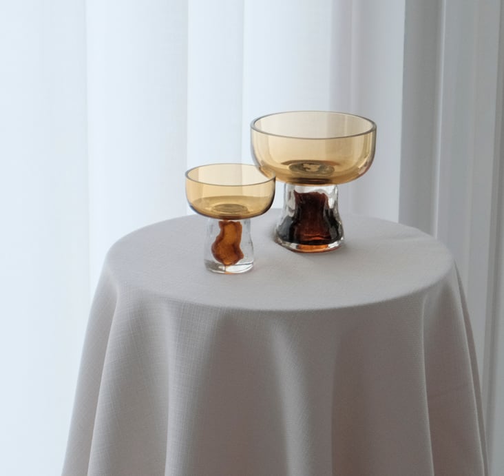 Two XLBoom 'Gusto' amber glass cups on a round table covered with a light grey linen cloth