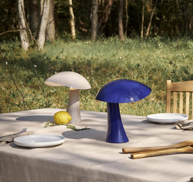 A blue and a yellow Louis Poulsen 'Rumee 220' mushroom lamp on an outdoor table at dusk