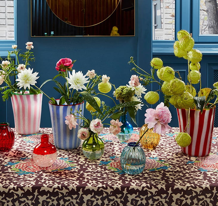 Colourful Lisa Corti vases filled with fresh flowers on a floral-print tablecloth