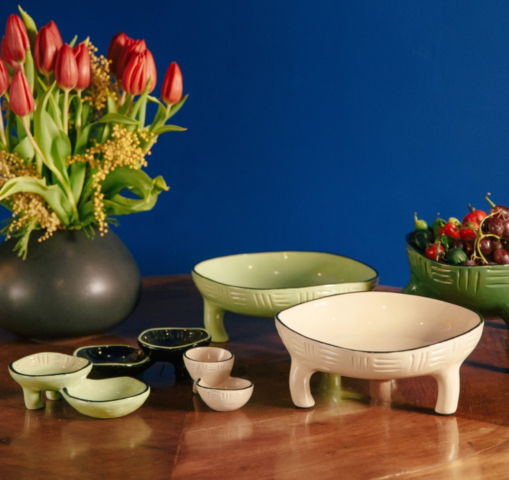 Pomax ceramic bowls and vases with tulips arranged on a wooden surface against a deep blue wall