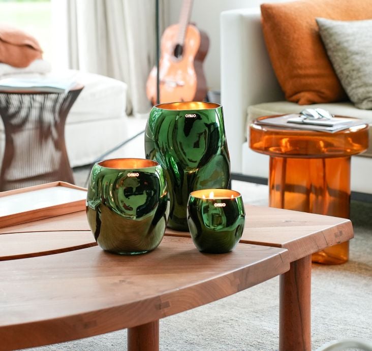 Three Onno Collection 'Cape' green glass candles of different sizes on a wooden coffee table in a warm living room