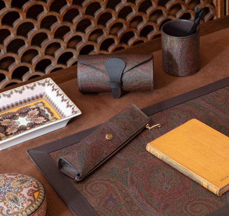 Etro Home leather accessories and printed textiles arranged on a dark wood surface
