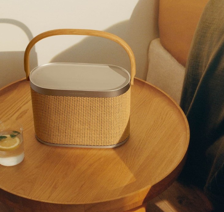 A Bang & Olufsen portable speaker in natural woven finish on a wooden side table
