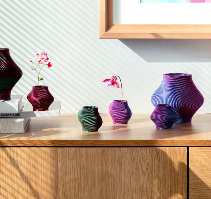 Five Sheyn ribbed vases in purple, pink, green and burgundy tones arranged on a wooden sideboard