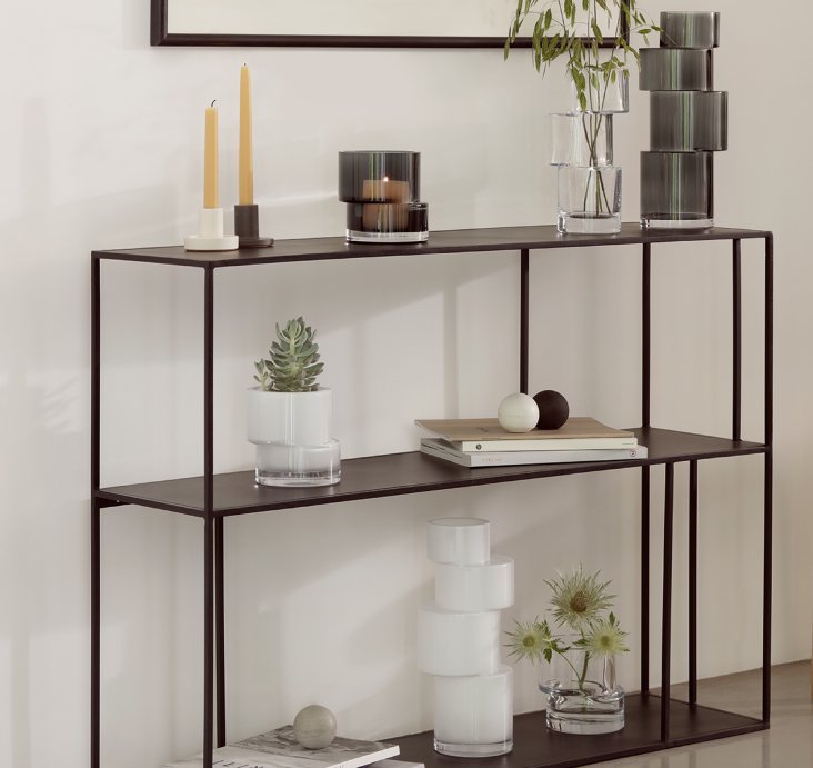 A slim black metal console table styled with candles, a plant and glassware in a minimal interior